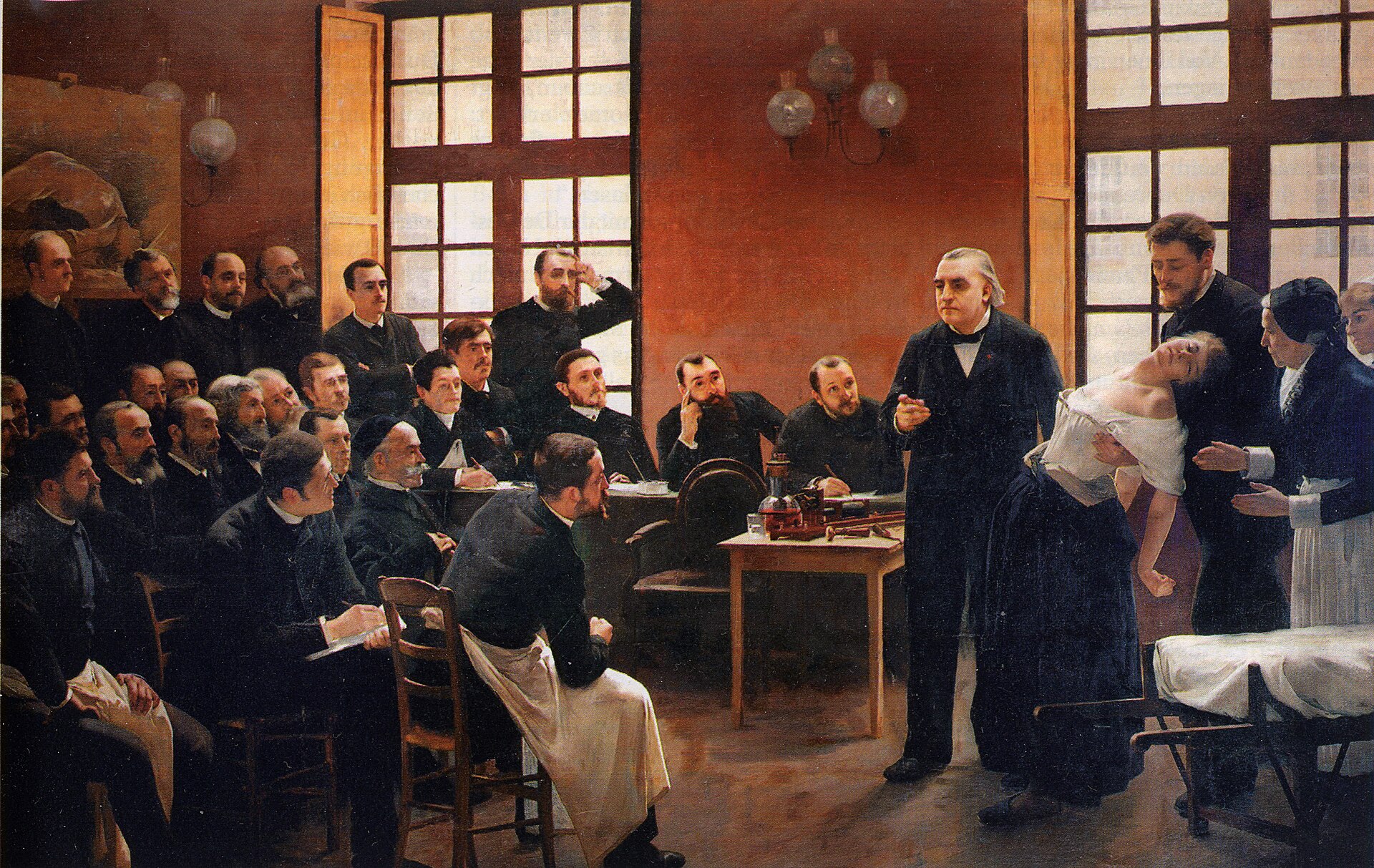 앙드레 브루예가 1887년에 그린 「살페트리에르의 임상 강의」입니다. 오른편에 홀로 서서 설명하는 흰머리 남성이 샤르코이고, 그 오른쪽에서 부축을 받고 있는 여성이 강의에 불려 나온 환자입니다 (위키미디어 공용, 퍼블릭 도메인)